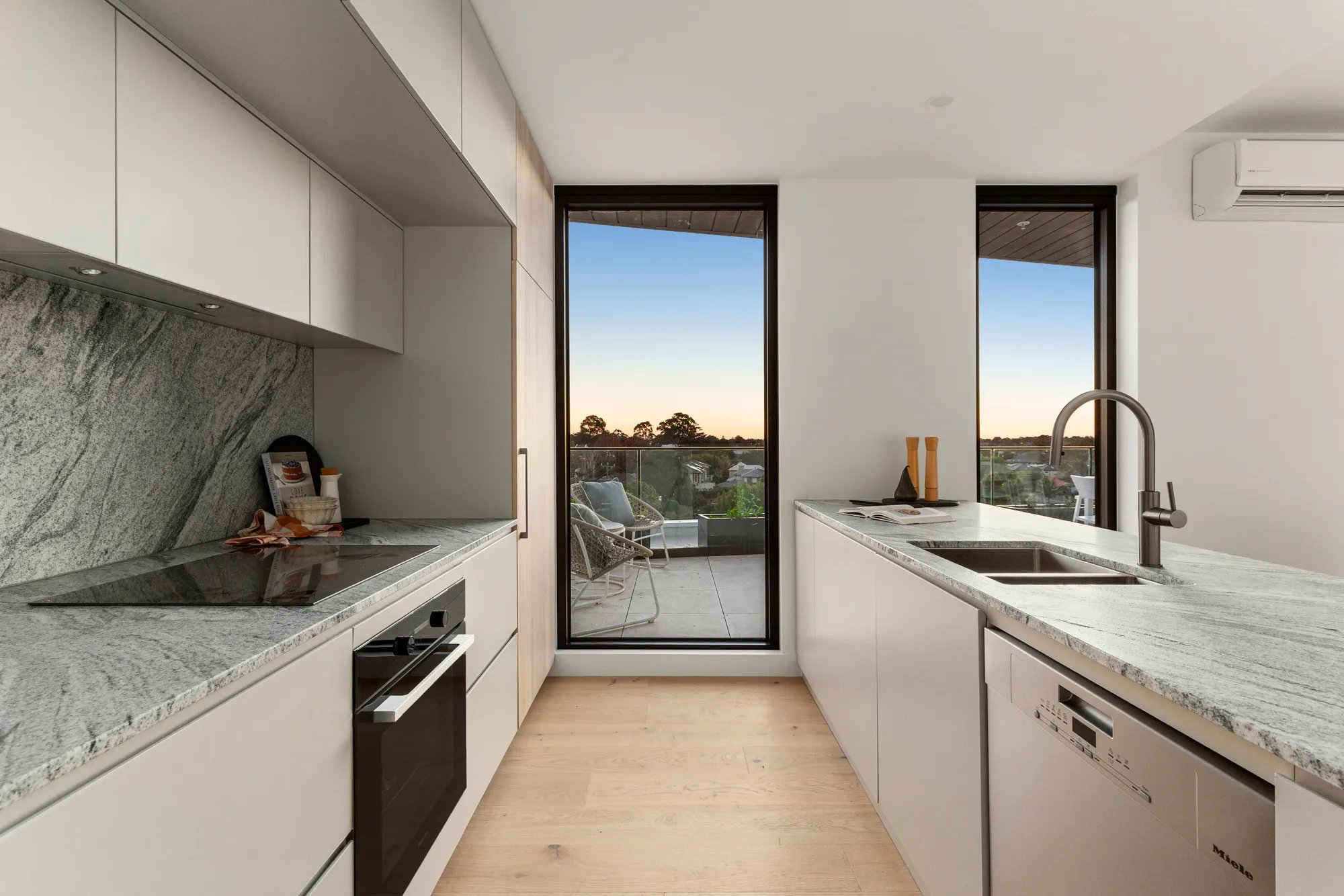 Kitchen with stone benchtops opening to a balcony at Iridian